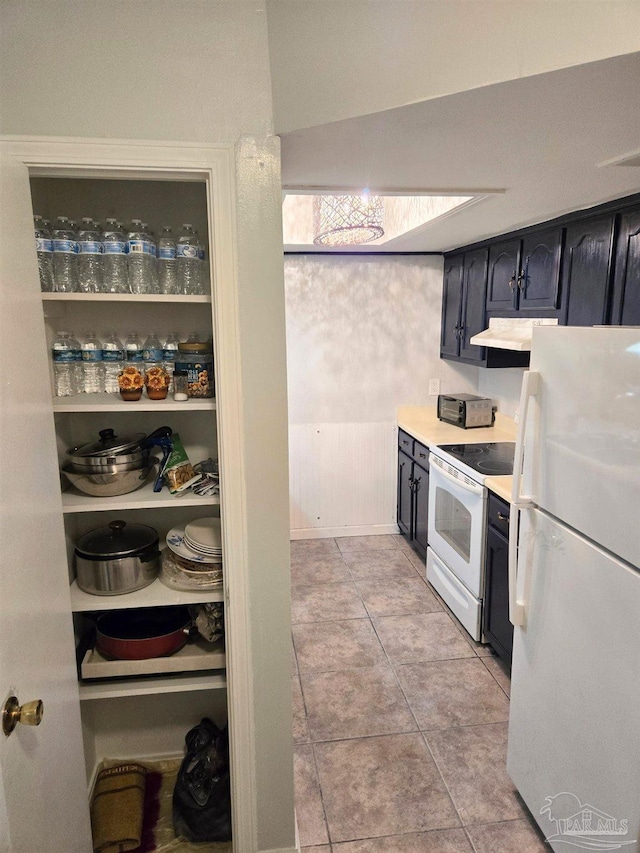 kitchen featuring white appliances, under cabinet range hood, light tile patterned floors, and light countertops