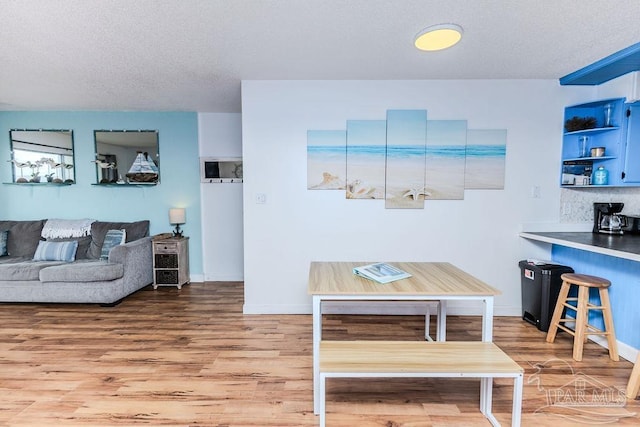 dining space with a textured ceiling, baseboards, and wood finished floors