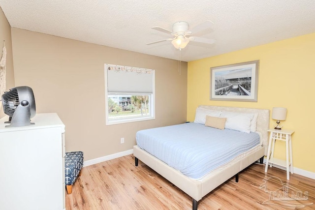 bedroom featuring light wood-style floors, ceiling fan, baseboards, and a textured ceiling