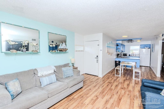 living room with light wood finished floors, visible vents, baseboards, and a textured ceiling