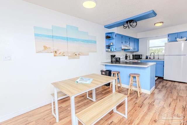 kitchen featuring stainless steel microwave, freestanding refrigerator, blue cabinets, under cabinet range hood, and open shelves