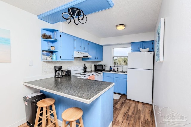 kitchen featuring under cabinet range hood, a peninsula, white appliances, a sink, and blue cabinetry