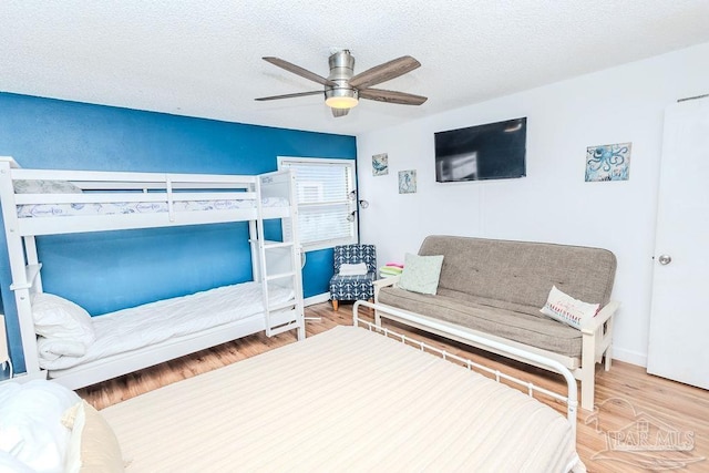 bedroom featuring ceiling fan, a textured ceiling, baseboards, and wood finished floors