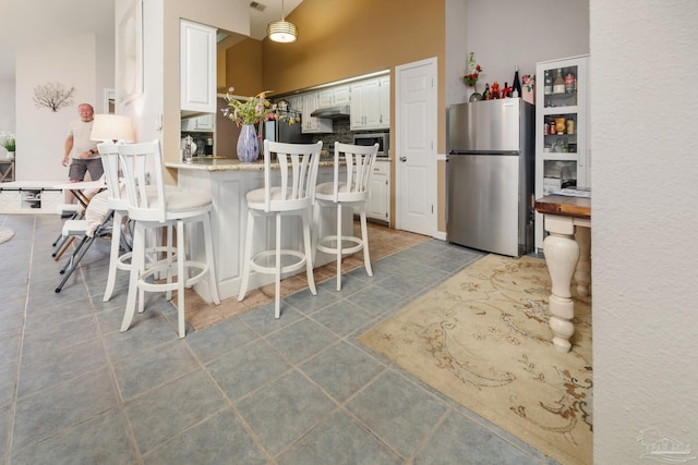 kitchen with a kitchen breakfast bar, kitchen peninsula, stainless steel appliances, white cabinets, and a towering ceiling