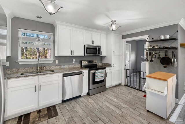 kitchen with appliances with stainless steel finishes, light wood-type flooring, ornamental molding, sink, and white cabinetry