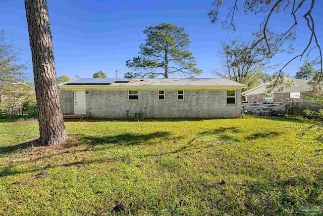 rear view of house with solar panels, a yard, and cooling unit