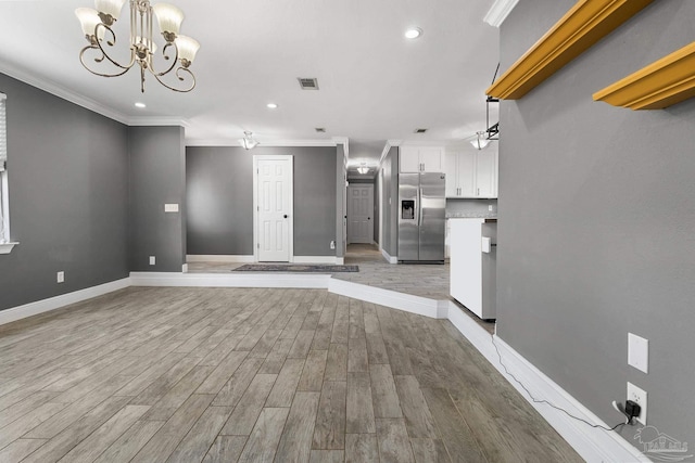 unfurnished living room featuring light wood-type flooring, crown molding, and an inviting chandelier