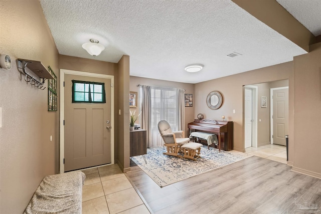 entryway with a textured ceiling, baseboards, visible vents, and light wood-style floors