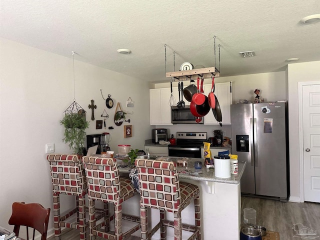 3464 Fallschase Blvd, Pensacola, FL 32526 - kitchen with appliances with stainless steel finishes, wood finished floors, white cabinets, a textured ceiling, and a breakfast bar area