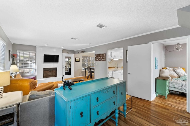 living room featuring sink, crown molding, a textured ceiling, hardwood / wood-style flooring, and a fireplace