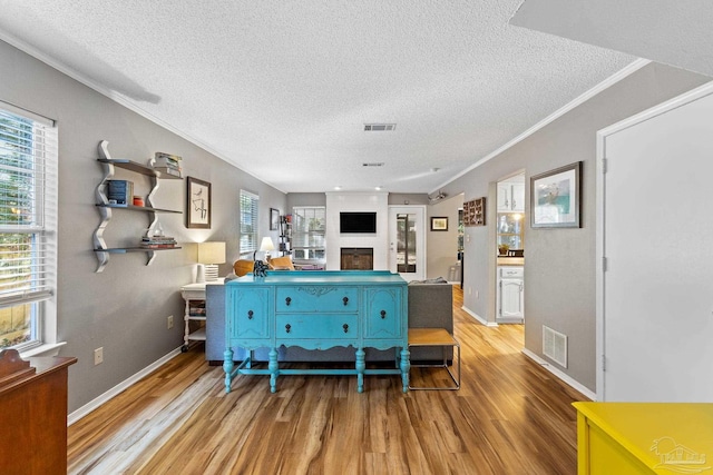 living room with a wealth of natural light, light hardwood / wood-style flooring, ornamental molding, and a textured ceiling