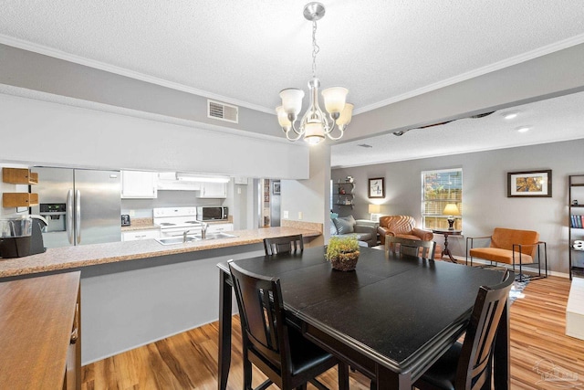 dining space with sink, light hardwood / wood-style flooring, an inviting chandelier, ornamental molding, and a textured ceiling