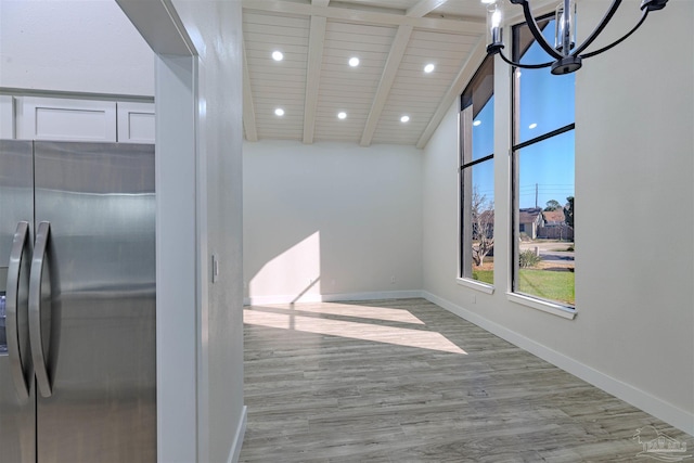 interior space featuring light wood-type flooring, a notable chandelier, beam ceiling, white cabinetry, and stainless steel refrigerator