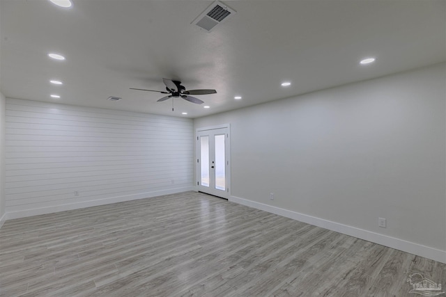 empty room with french doors, light hardwood / wood-style floors, ceiling fan, and wood walls