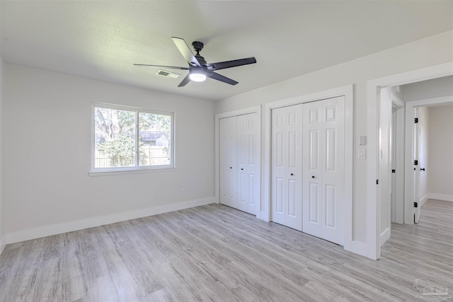 unfurnished bedroom featuring ceiling fan, light hardwood / wood-style floors, and two closets