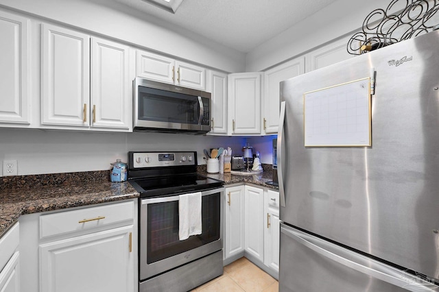 kitchen with white cabinets, appliances with stainless steel finishes, dark stone counters, and light tile patterned flooring