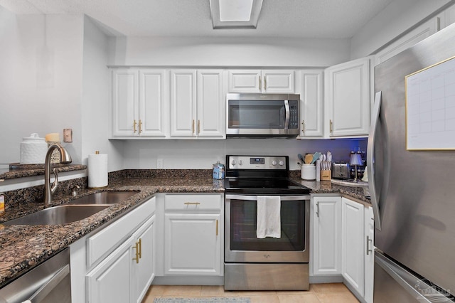 kitchen with appliances with stainless steel finishes, white cabinetry, sink, and dark stone counters