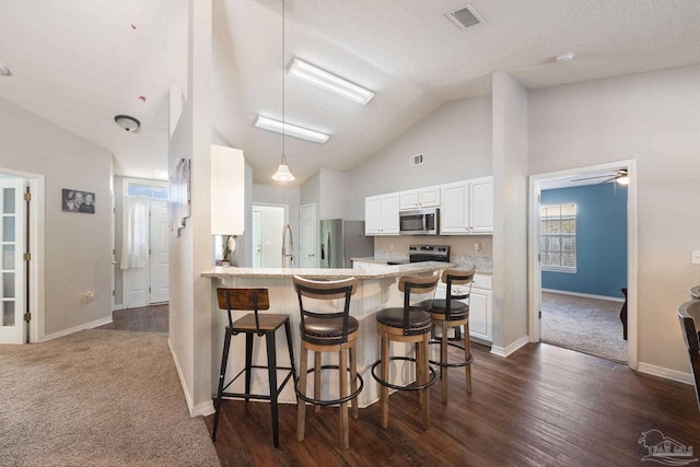 kitchen featuring lofted ceiling, stainless steel appliances, white cabinets, a kitchen bar, and kitchen peninsula