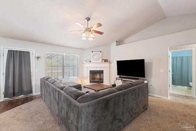 carpeted living room with ceiling fan, lofted ceiling, a textured ceiling, and a fireplace