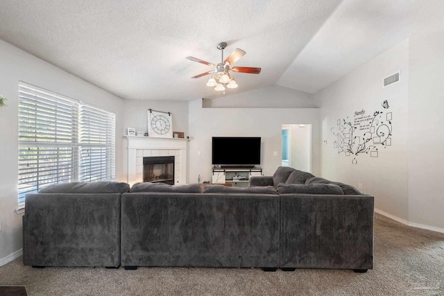 carpeted living room featuring a tile fireplace, lofted ceiling, a textured ceiling, and ceiling fan