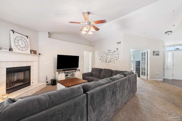 living room with a tile fireplace, ceiling fan, a textured ceiling, vaulted ceiling, and light colored carpet