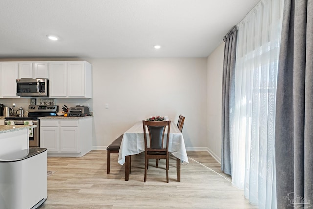kitchen with white cabinets, light stone counters, appliances with stainless steel finishes, and light hardwood / wood-style flooring