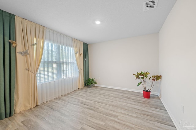 unfurnished room with a textured ceiling and light wood-type flooring