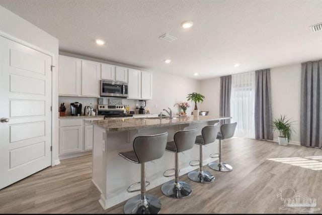 kitchen with a breakfast bar, appliances with stainless steel finishes, white cabinetry, and a kitchen island with sink