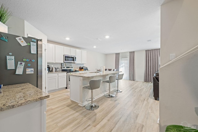 kitchen with a kitchen island with sink, light hardwood / wood-style flooring, appliances with stainless steel finishes, a kitchen bar, and white cabinetry