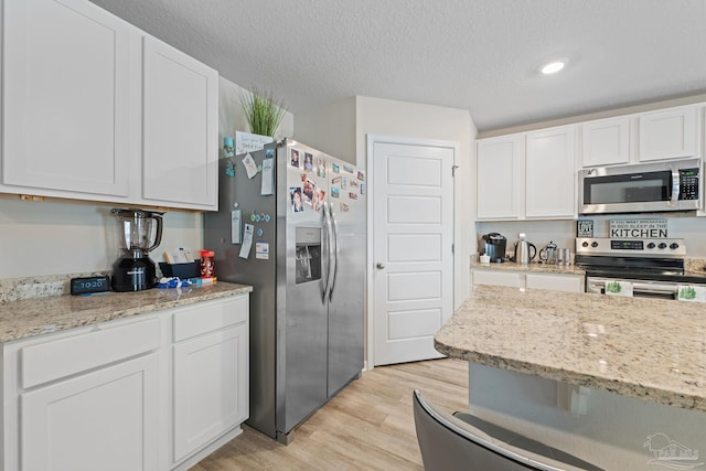 kitchen featuring a textured ceiling, light wood-type flooring, stainless steel appliances, and white cabinetry