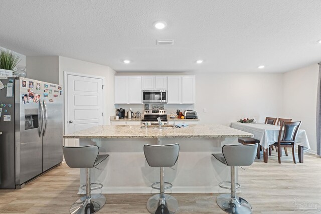 kitchen featuring light stone counters, a textured ceiling, a center island with sink, white cabinets, and appliances with stainless steel finishes