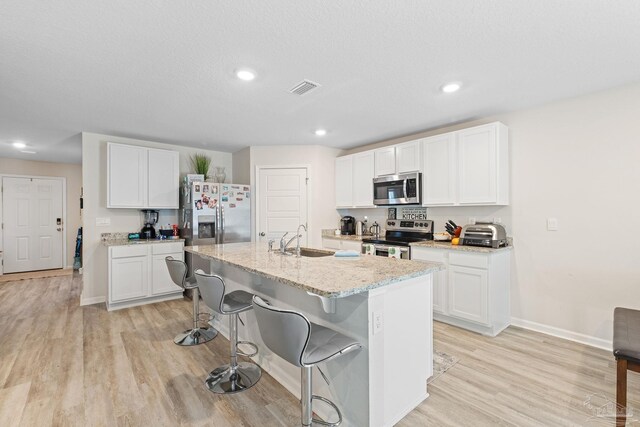 kitchen featuring light hardwood / wood-style flooring, white cabinetry, stainless steel appliances, and an island with sink