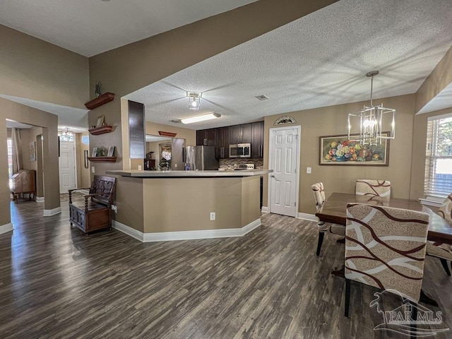 kitchen with appliances with stainless steel finishes, tasteful backsplash, dark brown cabinets, dark wood-type flooring, and a notable chandelier