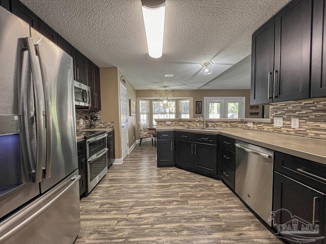 kitchen featuring kitchen peninsula, appliances with stainless steel finishes, tasteful backsplash, sink, and a chandelier