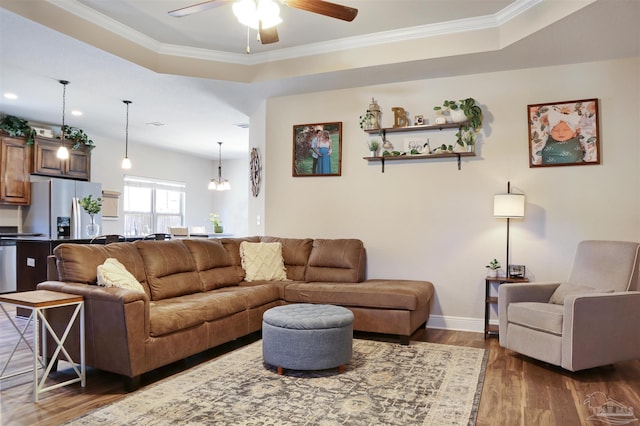 living area featuring dark wood finished floors, ceiling fan with notable chandelier, crown molding, and a raised ceiling