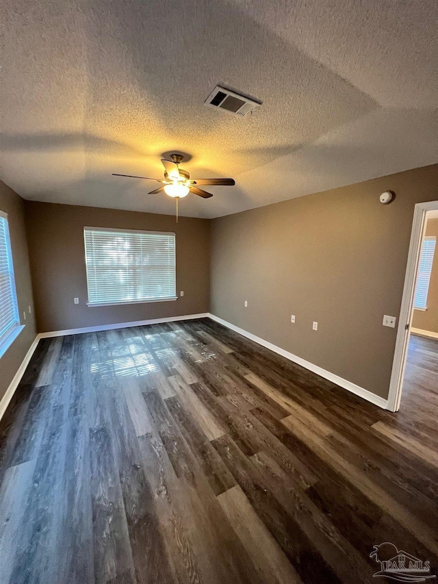 spare room with dark wood-type flooring, visible vents, and baseboards