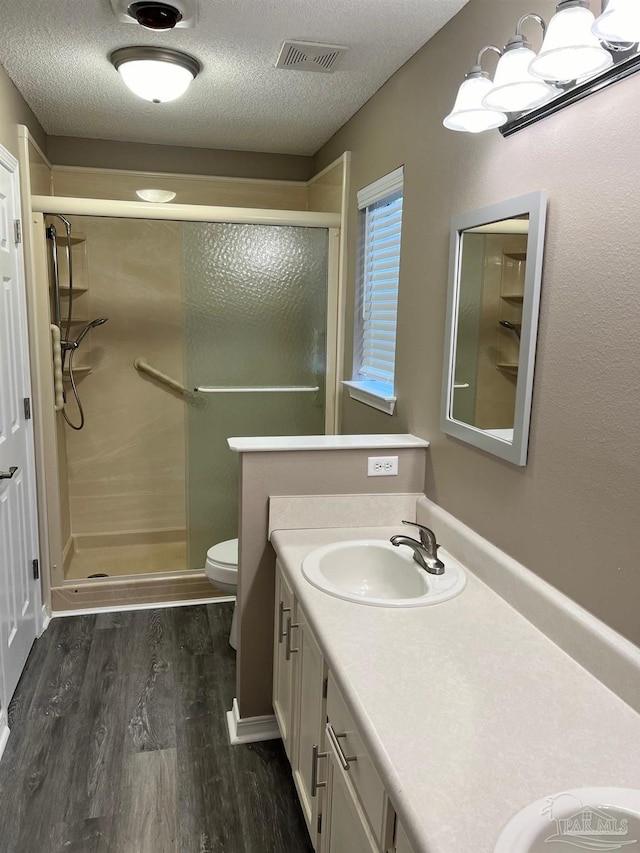 bathroom featuring visible vents, toilet, wood finished floors, a textured ceiling, and a shower stall