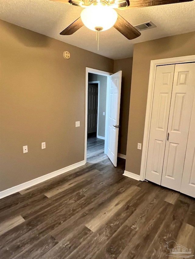 unfurnished bedroom with ceiling fan, a textured ceiling, visible vents, baseboards, and dark wood-style floors