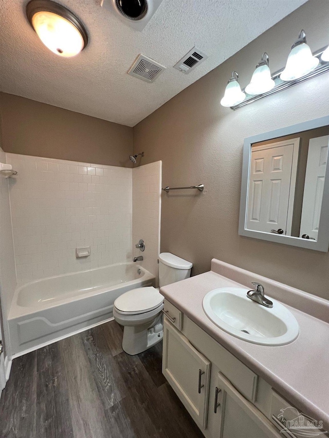 bathroom featuring a textured ceiling, shower / bathtub combination, wood finished floors, and toilet