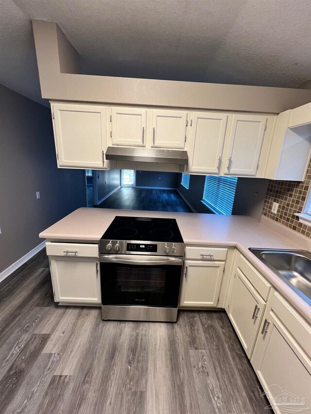 kitchen with dark wood-style flooring, light countertops, stainless steel range with electric cooktop, white cabinets, and under cabinet range hood