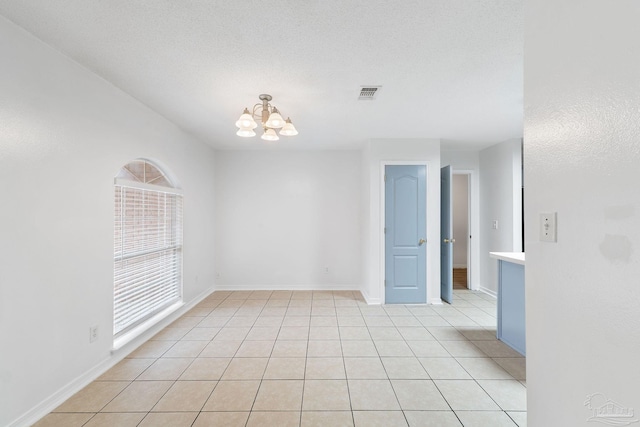 tiled spare room featuring a textured ceiling and a notable chandelier