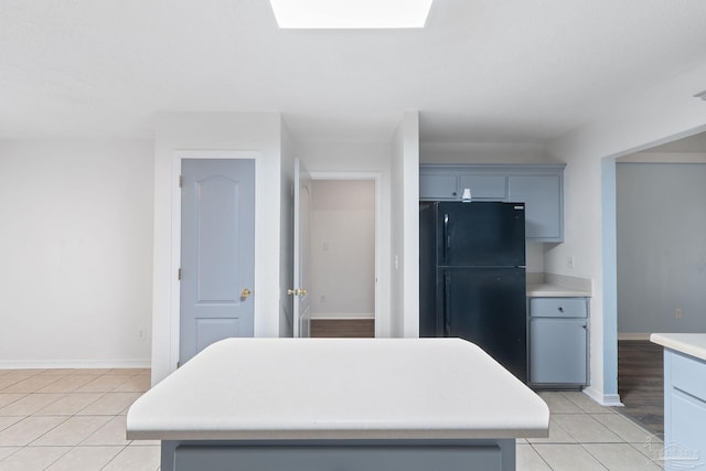 kitchen with gray cabinets, a skylight, a center island, light tile patterned floors, and black fridge