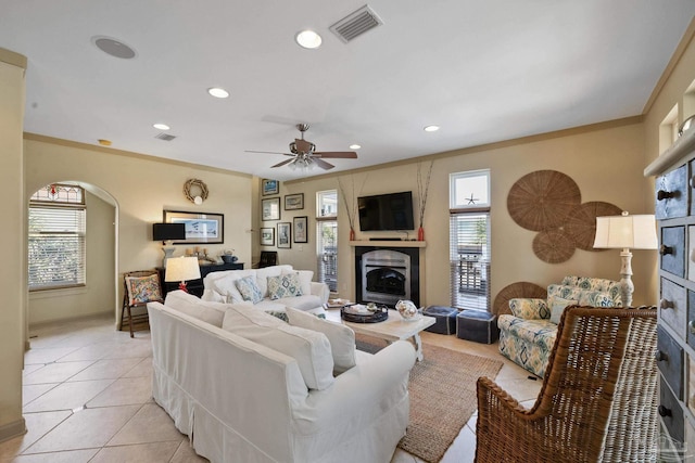 tiled living room with ceiling fan, ornamental molding, and a fireplace