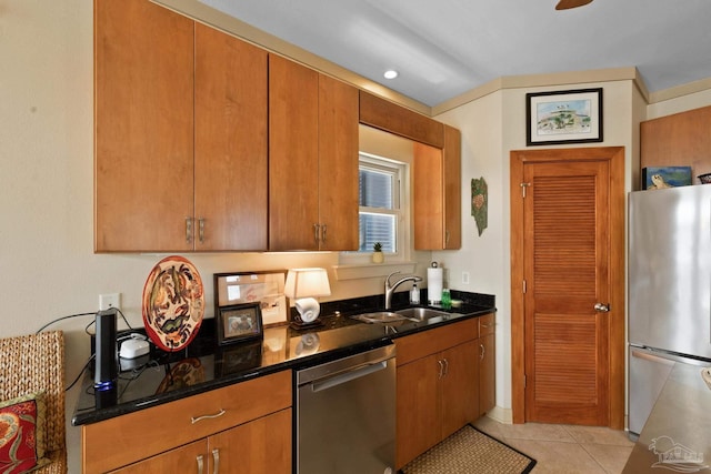 kitchen with light tile patterned flooring, appliances with stainless steel finishes, dark stone counters, and sink