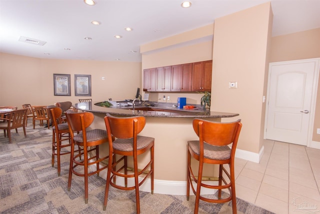 kitchen featuring light tile patterned flooring, recessed lighting, a peninsula, a breakfast bar, and dark countertops