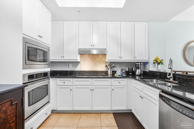 kitchen featuring stainless steel appliances, white cabinets, a sink, dark stone countertops, and under cabinet range hood