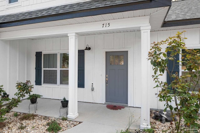 view of exterior entry featuring covered porch, board and batten siding, and a shingled roof