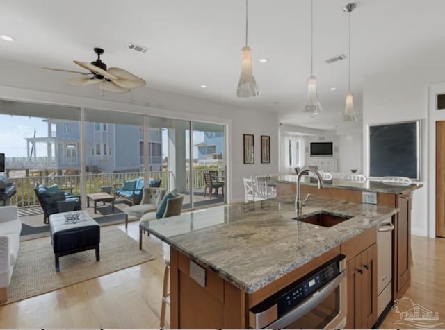 kitchen featuring pendant lighting, sink, light stone counters, a center island with sink, and light wood-type flooring