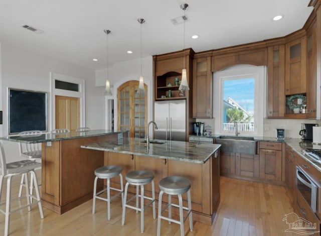 kitchen featuring appliances with stainless steel finishes, dark stone countertops, hanging light fixtures, a kitchen breakfast bar, and an island with sink