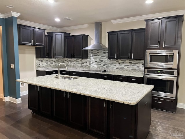 kitchen with sink, ornamental molding, a kitchen island with sink, stainless steel appliances, and wall chimney range hood